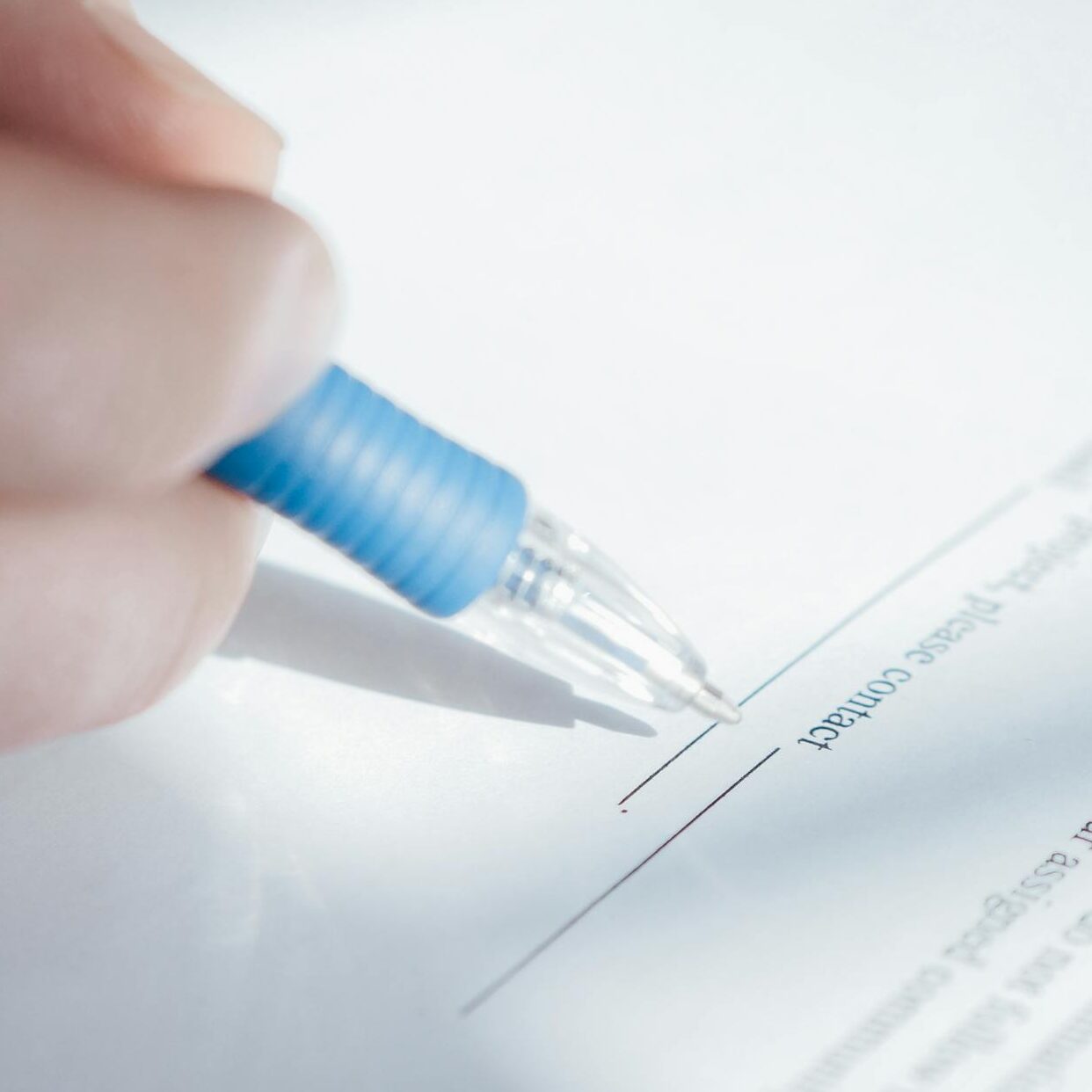 A close-up image showing a hand holding a pen while signing a document.